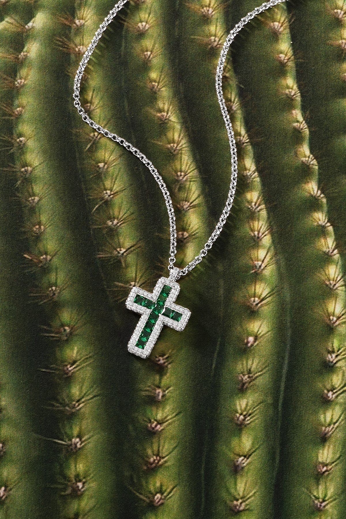 Silver cross necklace with green stones on a cactus background