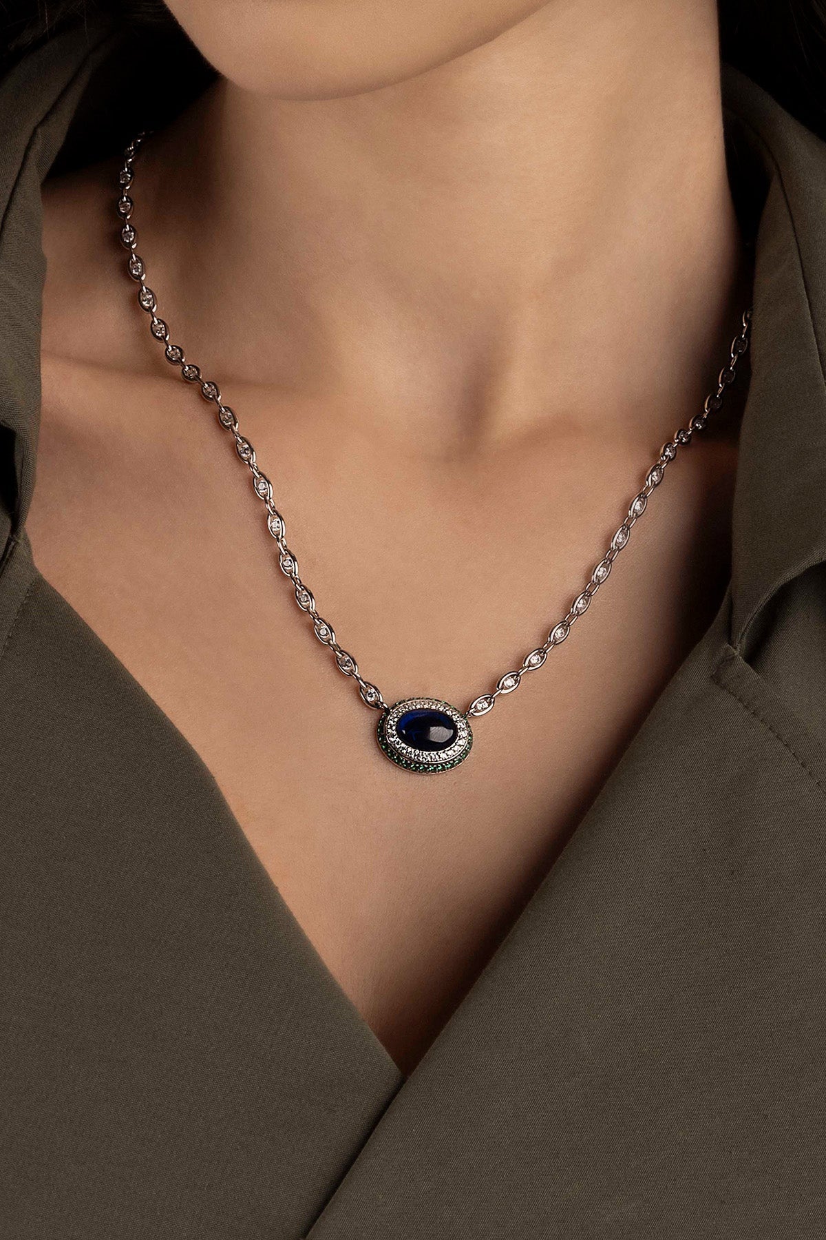 Necklace with a blue stone pendant worn by a model in a brown outfit.