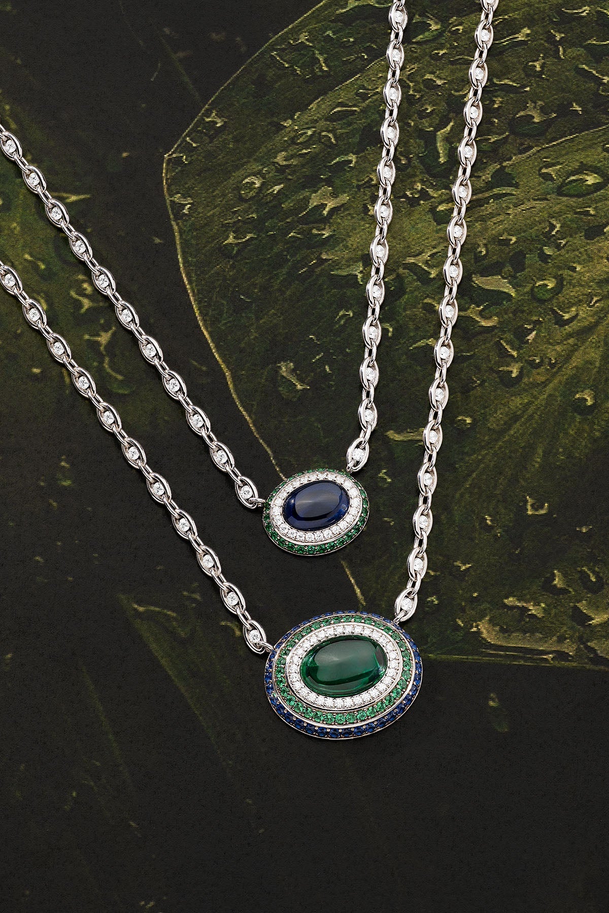 Two silver necklaces with gemstone pendants on a dark leafy background