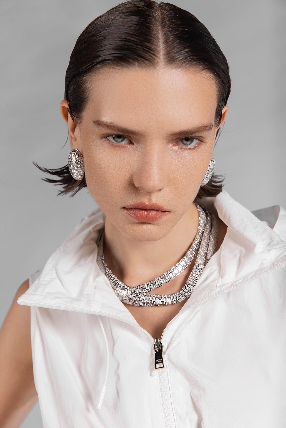 Woman wearing a white outfit with APM MONACO labyrinth silver necklace and earrings against a gray background