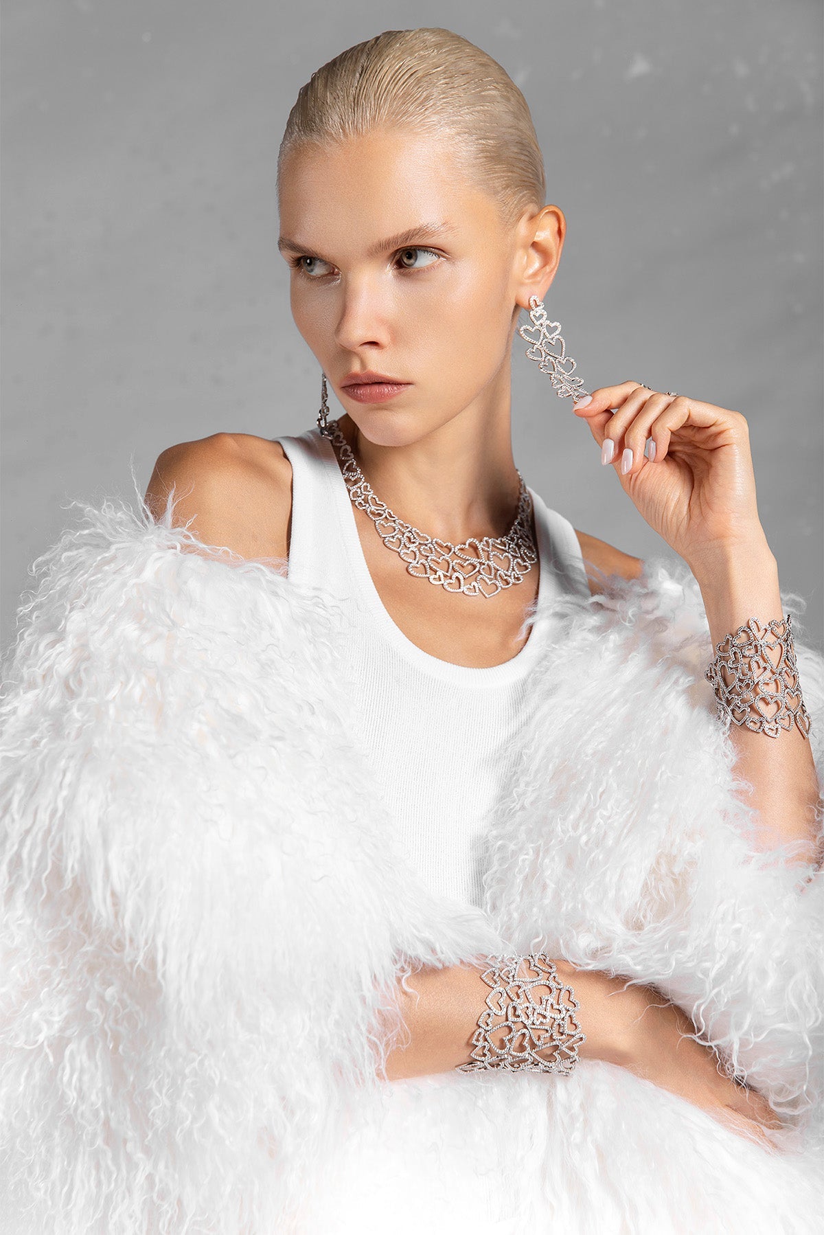 Woman wearing a white dress with APM MONACO heart-shaped jewelry against a gray background