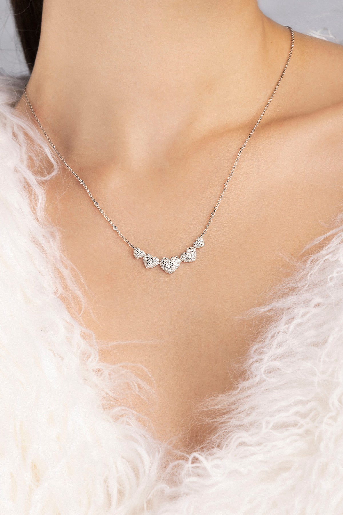 APM MONACO necklace in silver with heart-shaped pendants on a model wearing a white fur garment