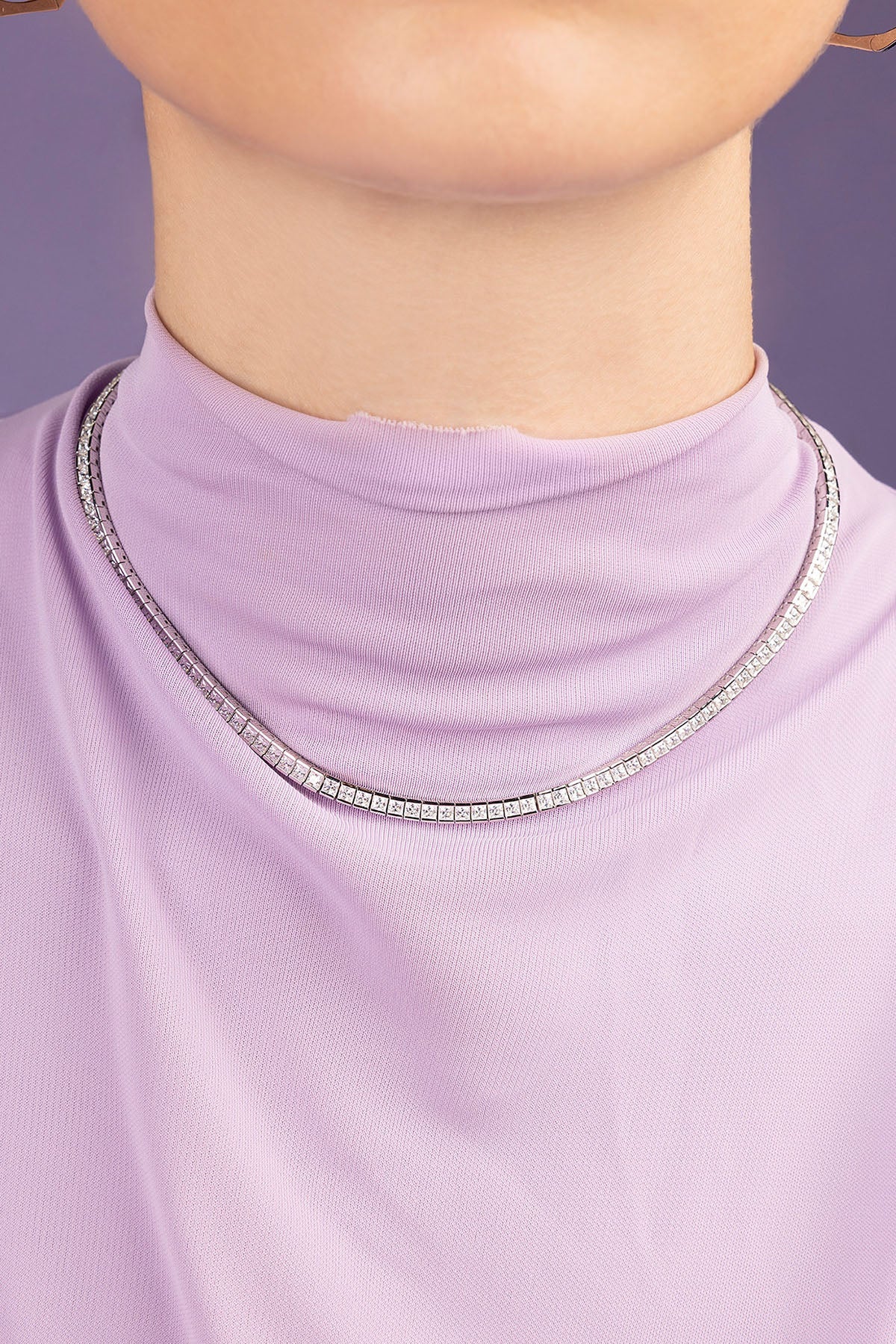 Close-up of a person wearing a light purple turtleneck with a silver necklace.