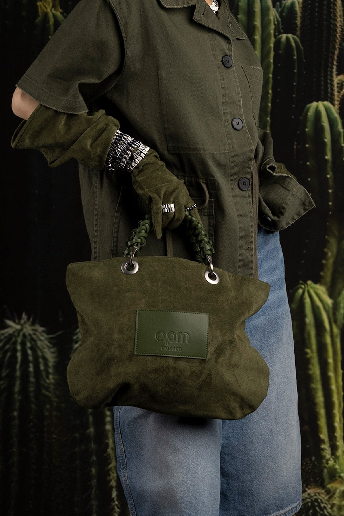 Model holding a green suede handbag with cacti in the background