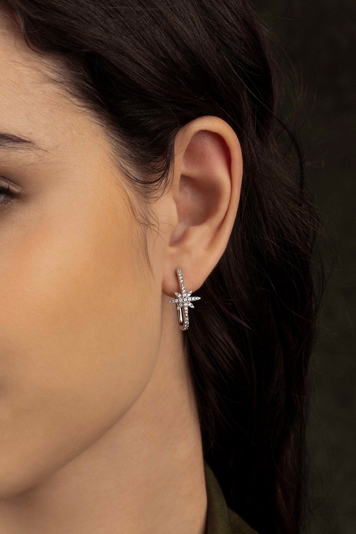 Close-up of a woman wearing a silver star-shaped earring against a dark background