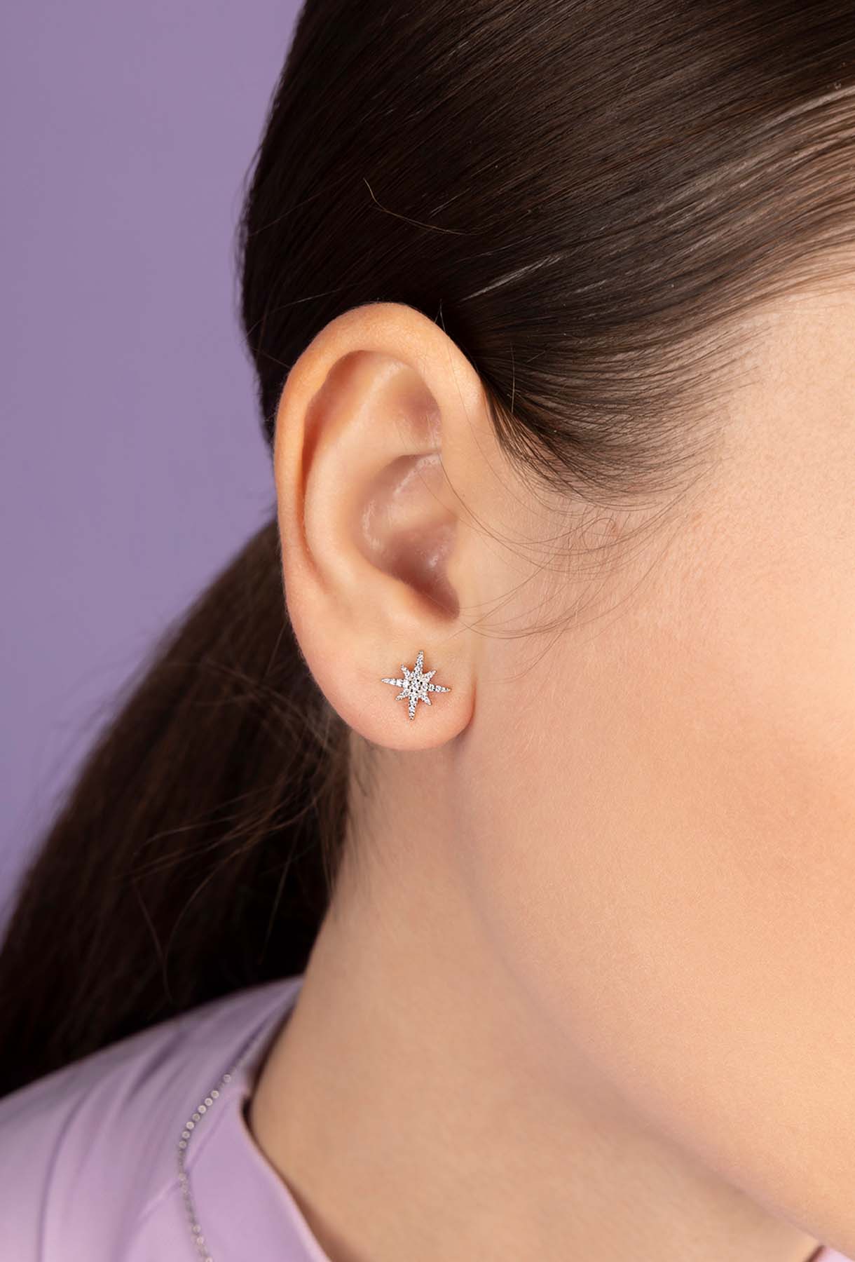 Close-up of an ear wearing a star-shaped earring with a purple background