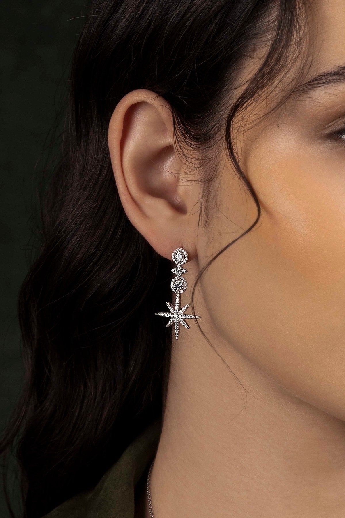 Close-up of a person wearing a silver star-shaped earring against a dark background
