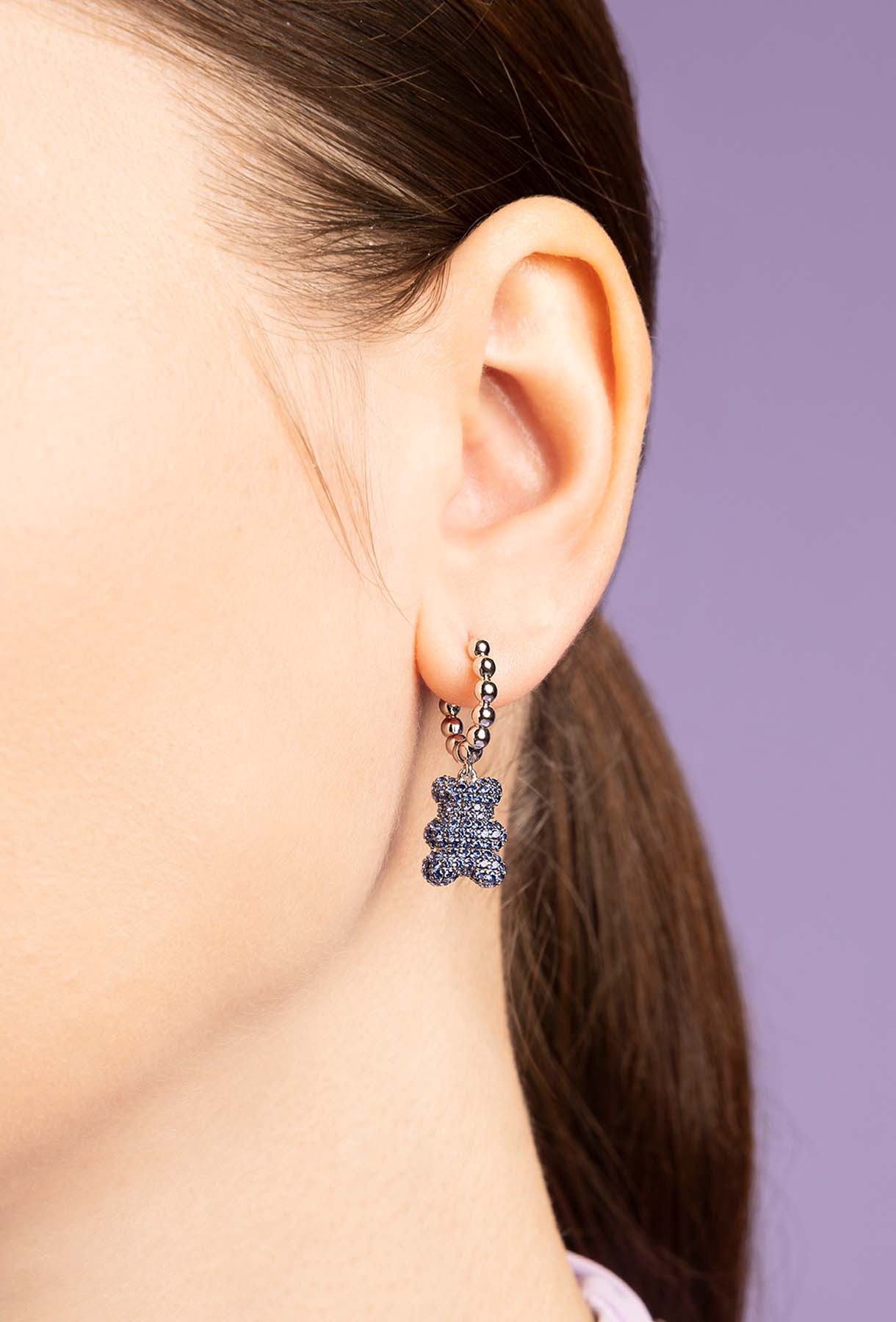Close-up of a person wearing a unique earring with a purple gemstone on a plain background