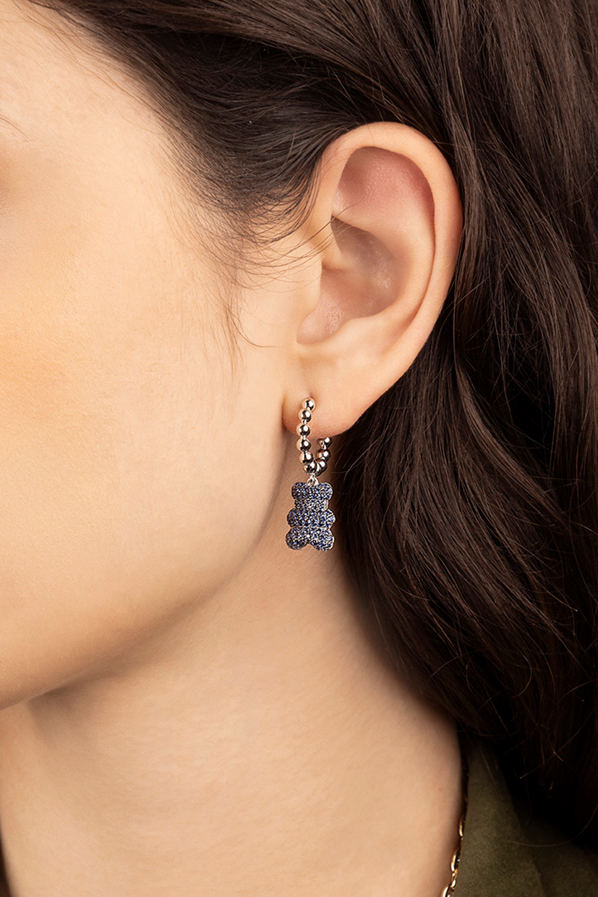 Close-up of a person wearing APM MONACO sparkling YUMMY BEAR SHAPED earring with a blurred background