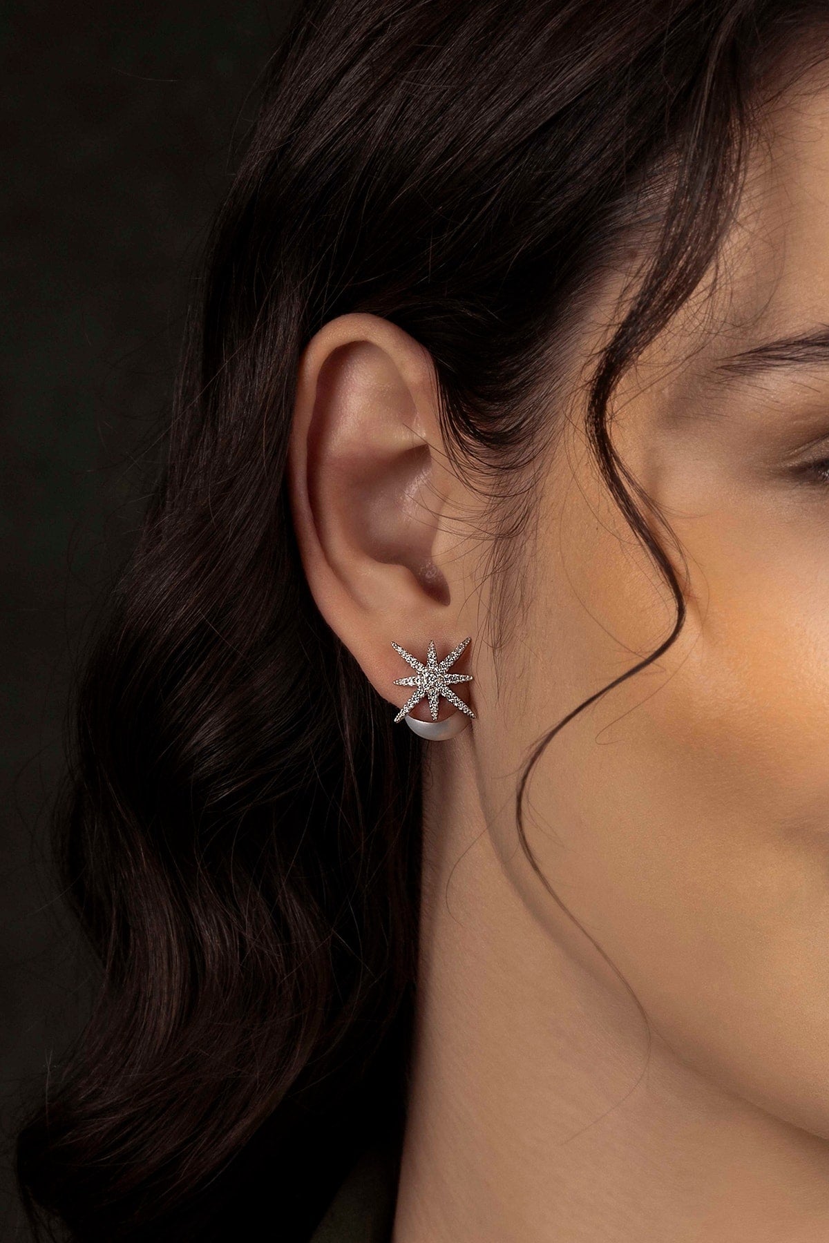 Close-up of a person wearing a star-shaped earring with a dark background