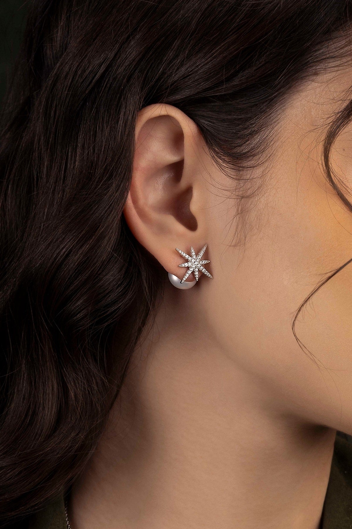 Close-up of an ear wearing a star-shaped earring with dark hair and skin in the background