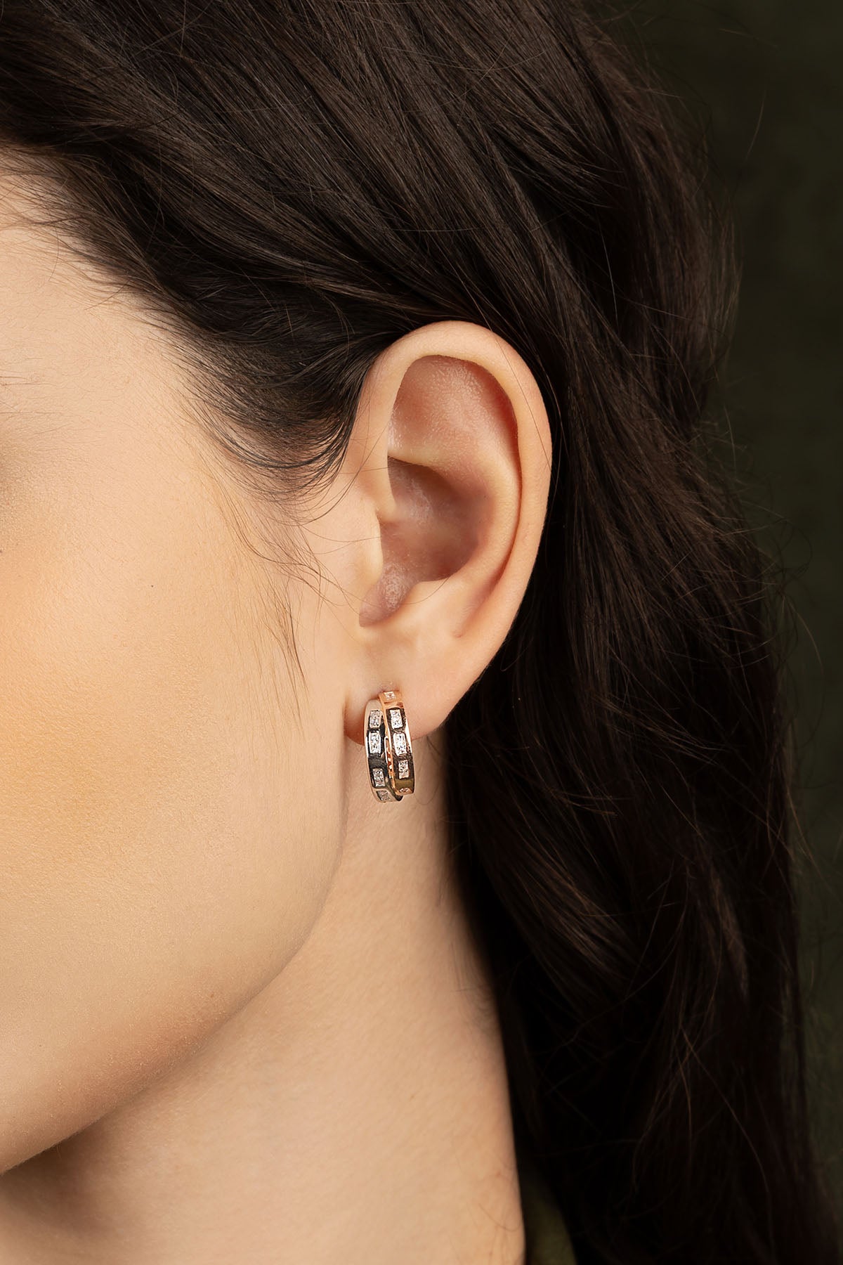 Close-up of an ear wearing a gold hoop earring with a dark background