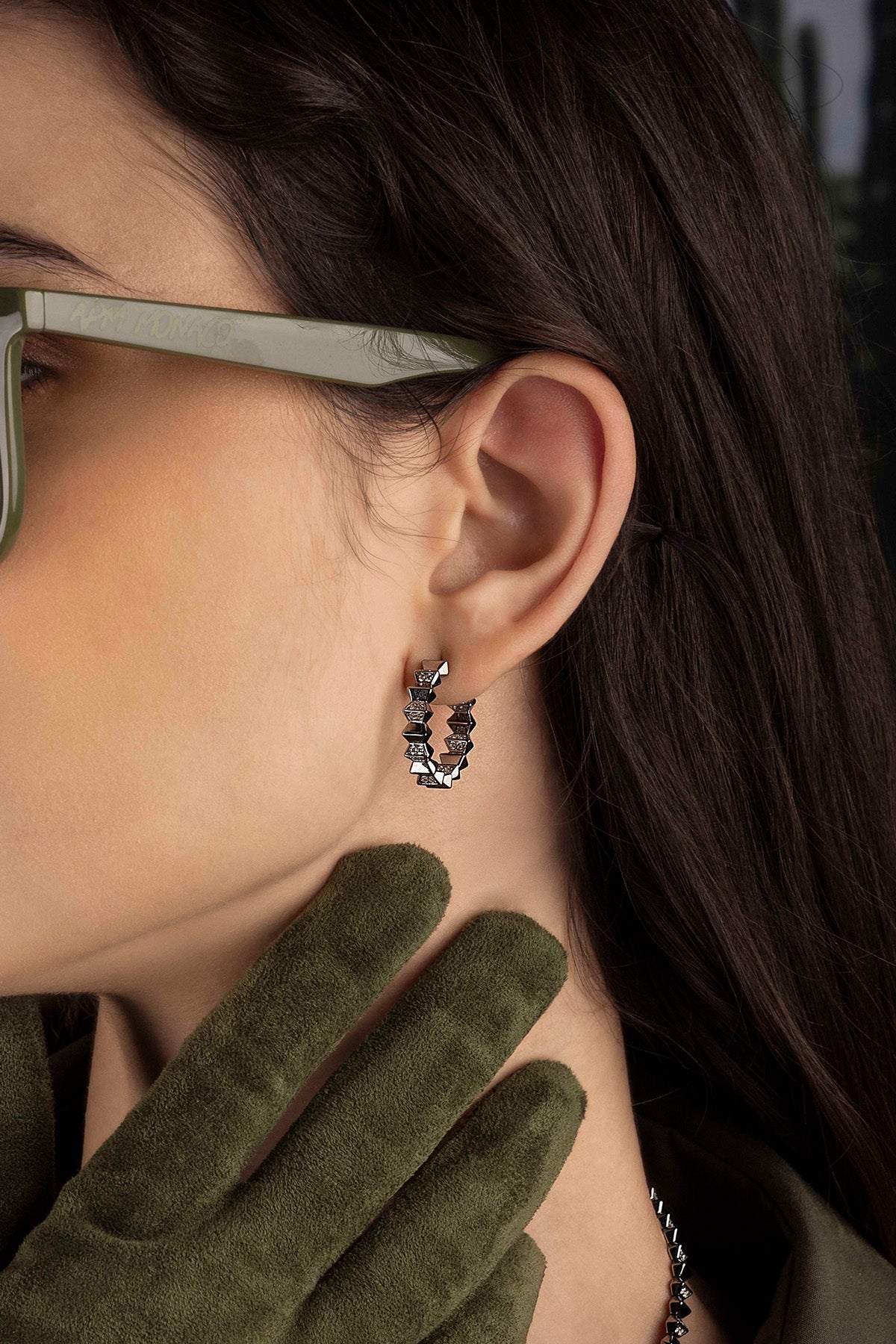 Close-up of a model wearing hoop earrings, green gloves, and sunglasses.