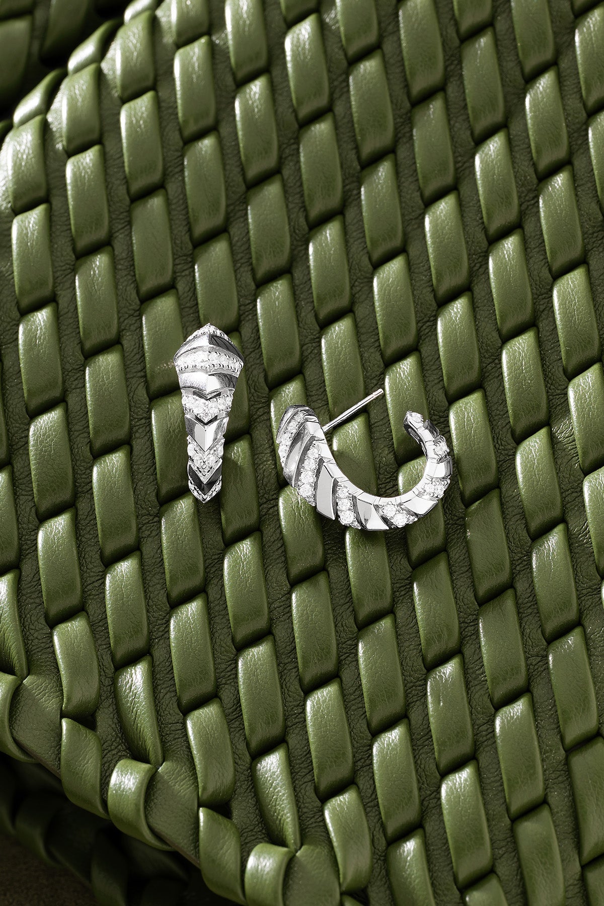 Silver earrings on a green surface background