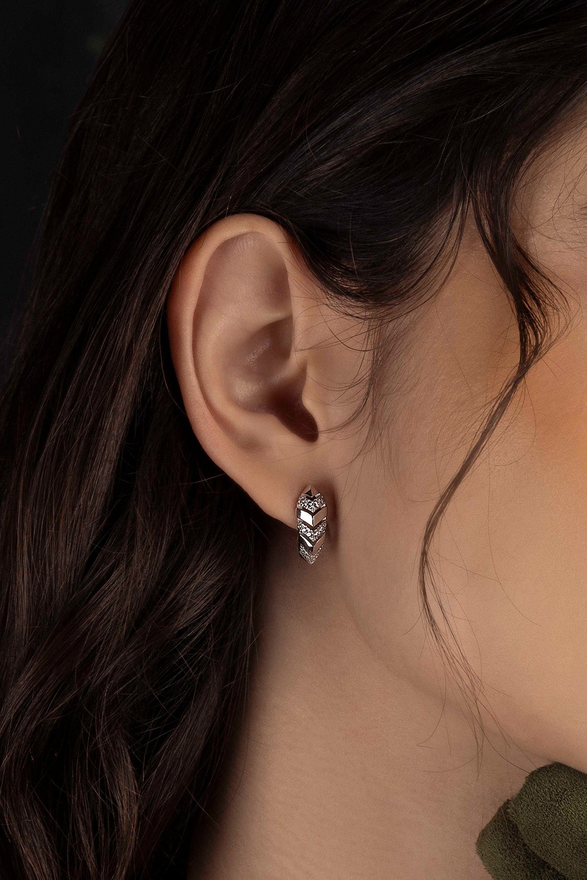 Close-up of an ear wearing a silver earring with a dark background