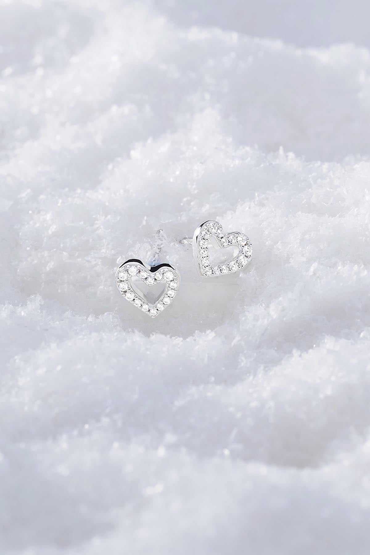 APM MONACO heart-shaped earrings with clear stones on a snowy textured surface