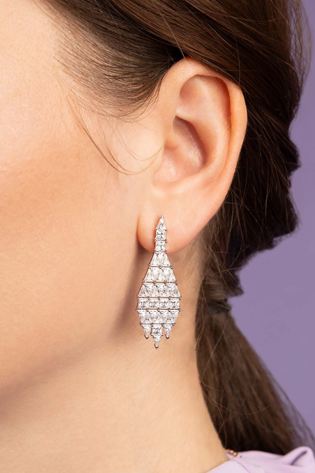 Close-up of a person wearing a sparkling earring against a purple background