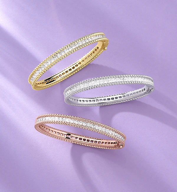 Three APM MONACO new-in bangles in yellow gold, silver, and rose gold on a purple background
