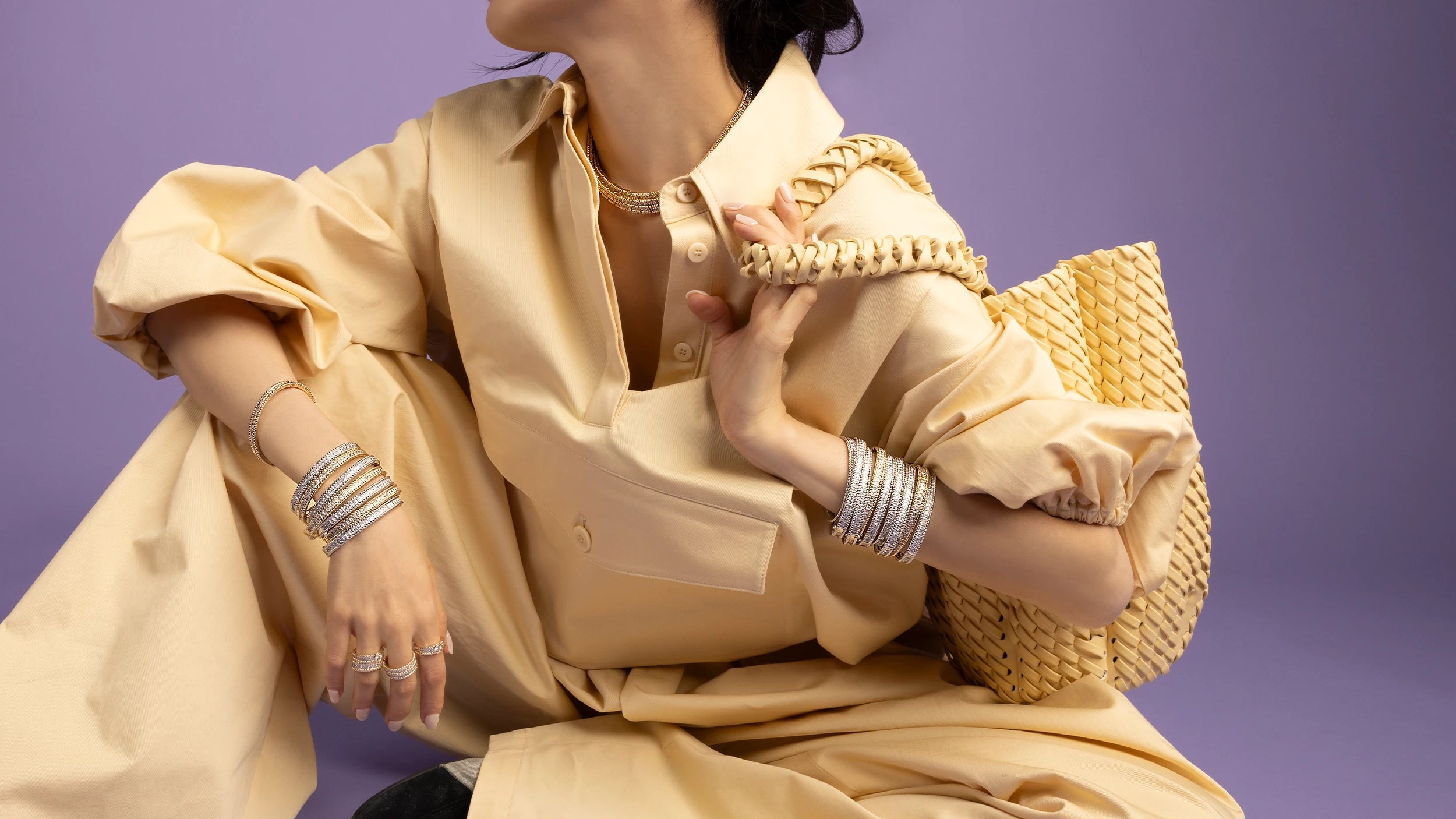 Person wearing a yellow outfit with APM MONACO silver and yellow-gold color jewelry set from Printemps collection against a purple background