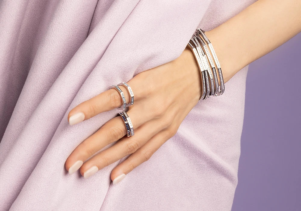 Hand wearing multiple APM MONACO Printemps silver rings and bracelets on a light purple fabric background