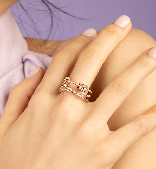 Close-up of a hand wearing two APM MONACO rose gold rings on a blurred background