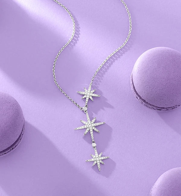 APM MONACO silver star-shaped necklace on a purple surface with macarons