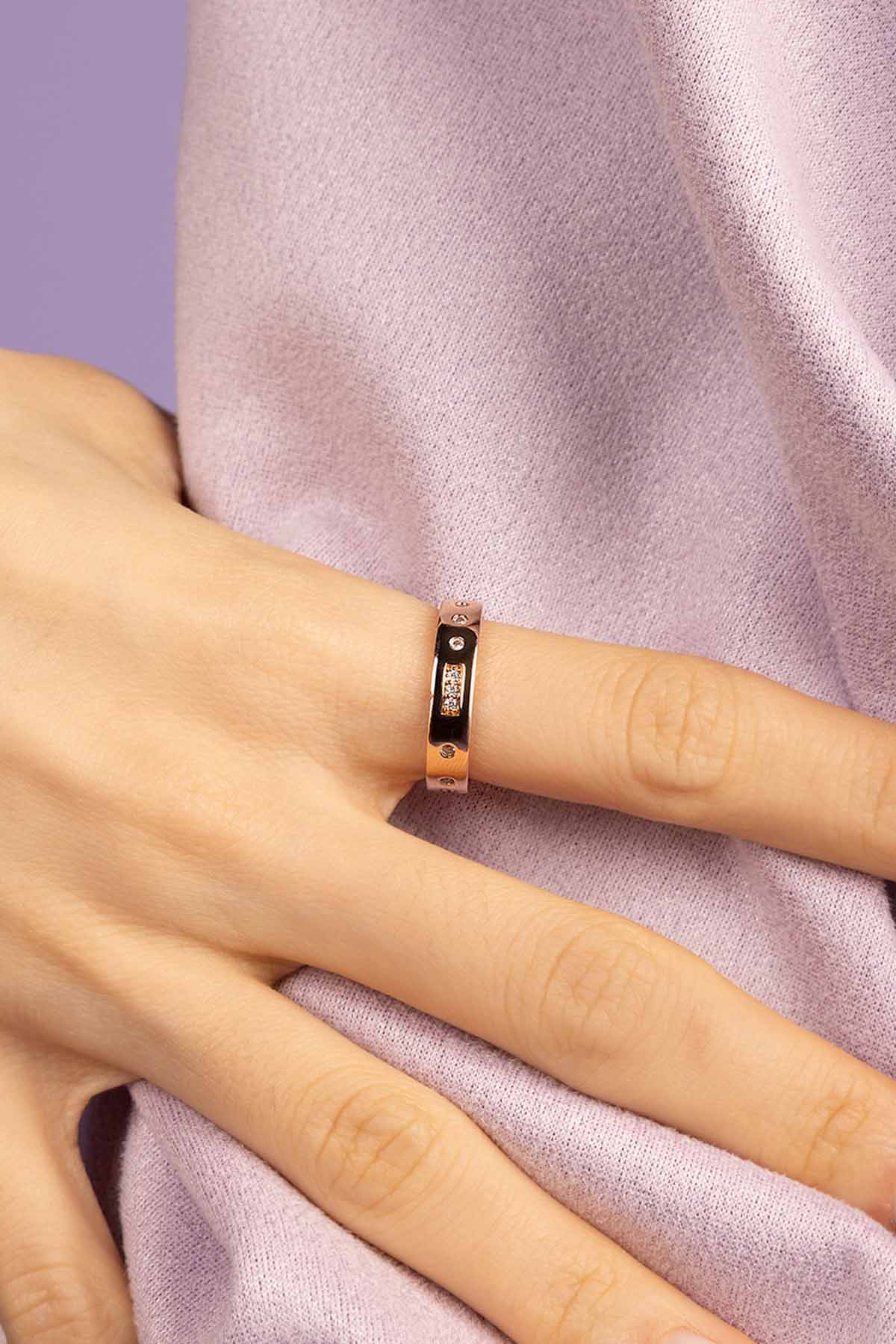 Rose gold ring on a person's finger against a light purple fabric background