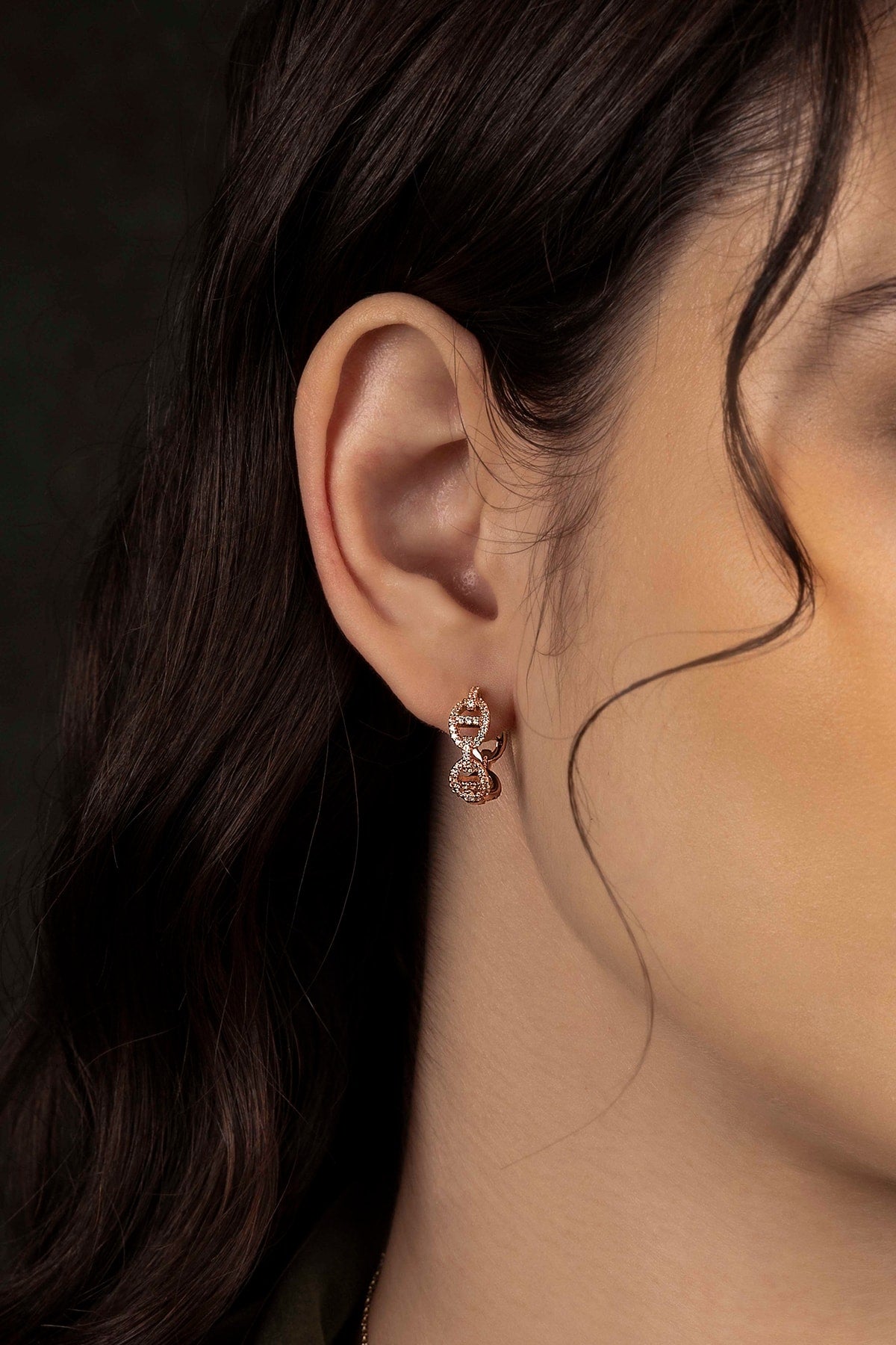 Close-up of an ear wearing a delicate earring with a dark background