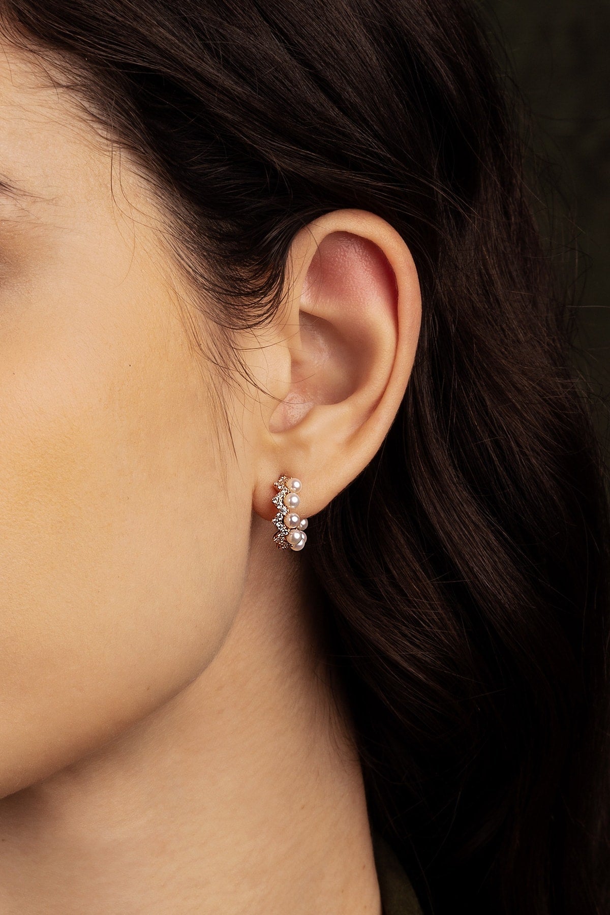 Close-up of an ear wearing a pearl earring with a dark background
