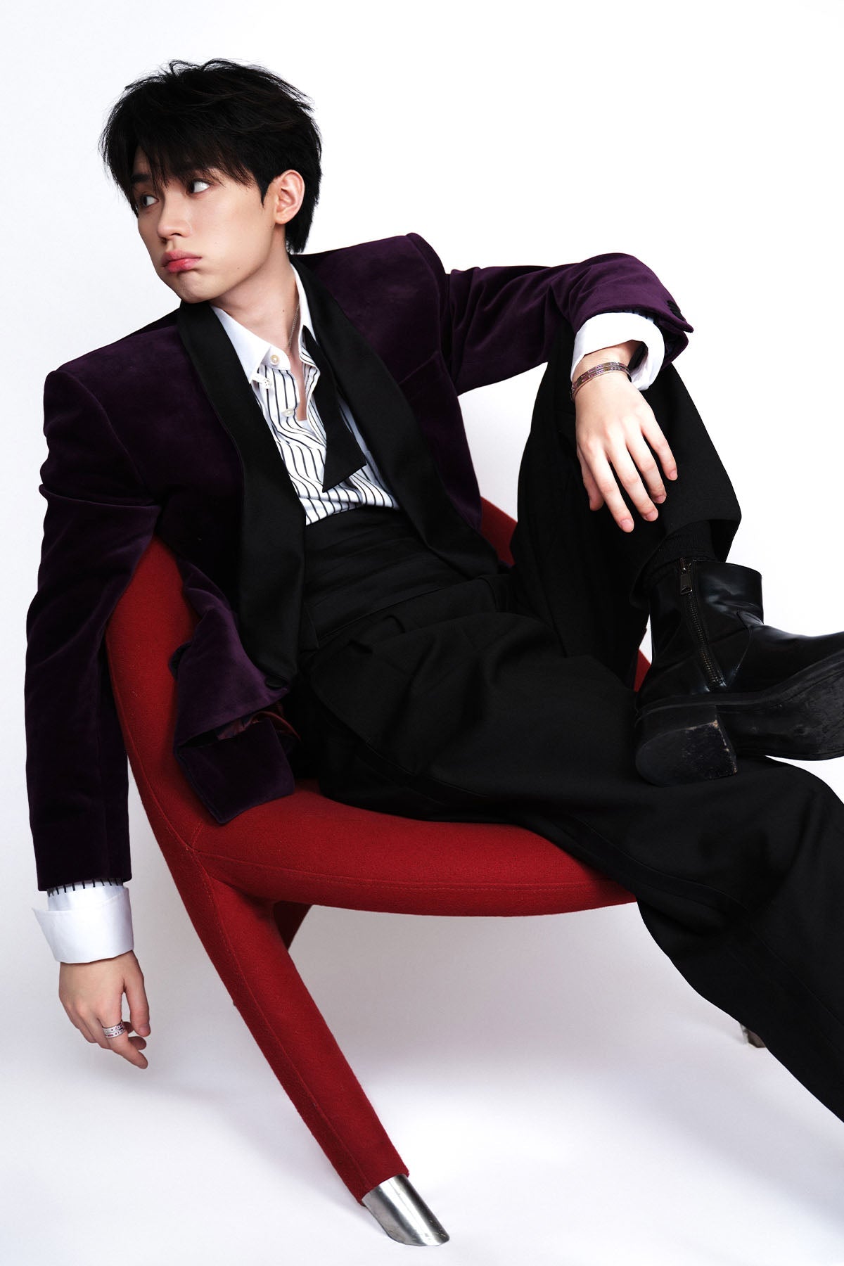 Model wearing a black suit with a purple blazer with jewelry sitting on a chair.