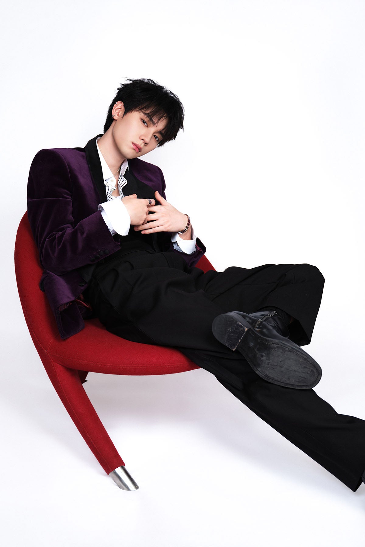 Model in a purple suit with ring and bangle sitting on a red chair against a white background