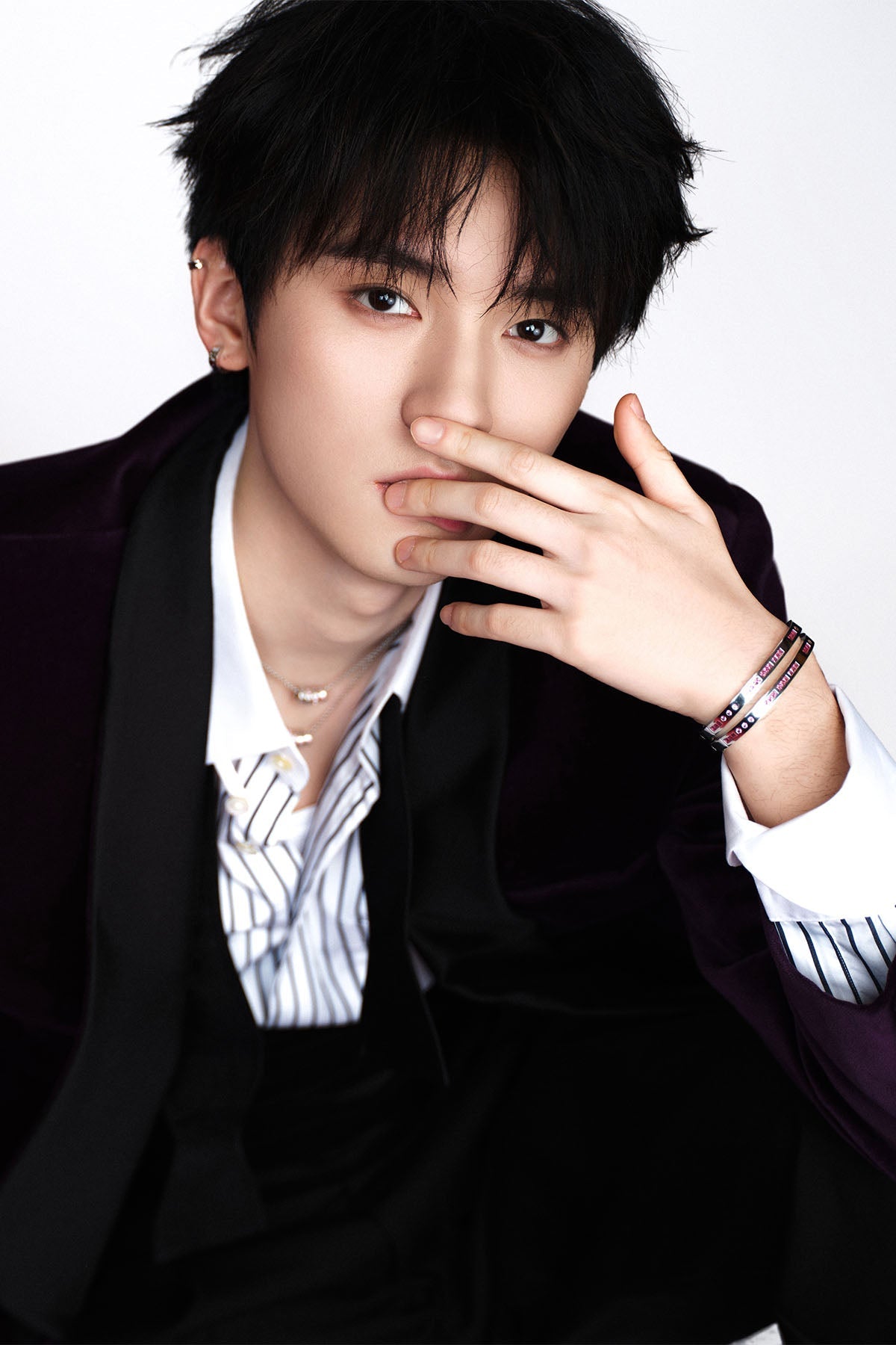 Man wearing a dark suit with a white shirt and striped tie, posing with hand on face.