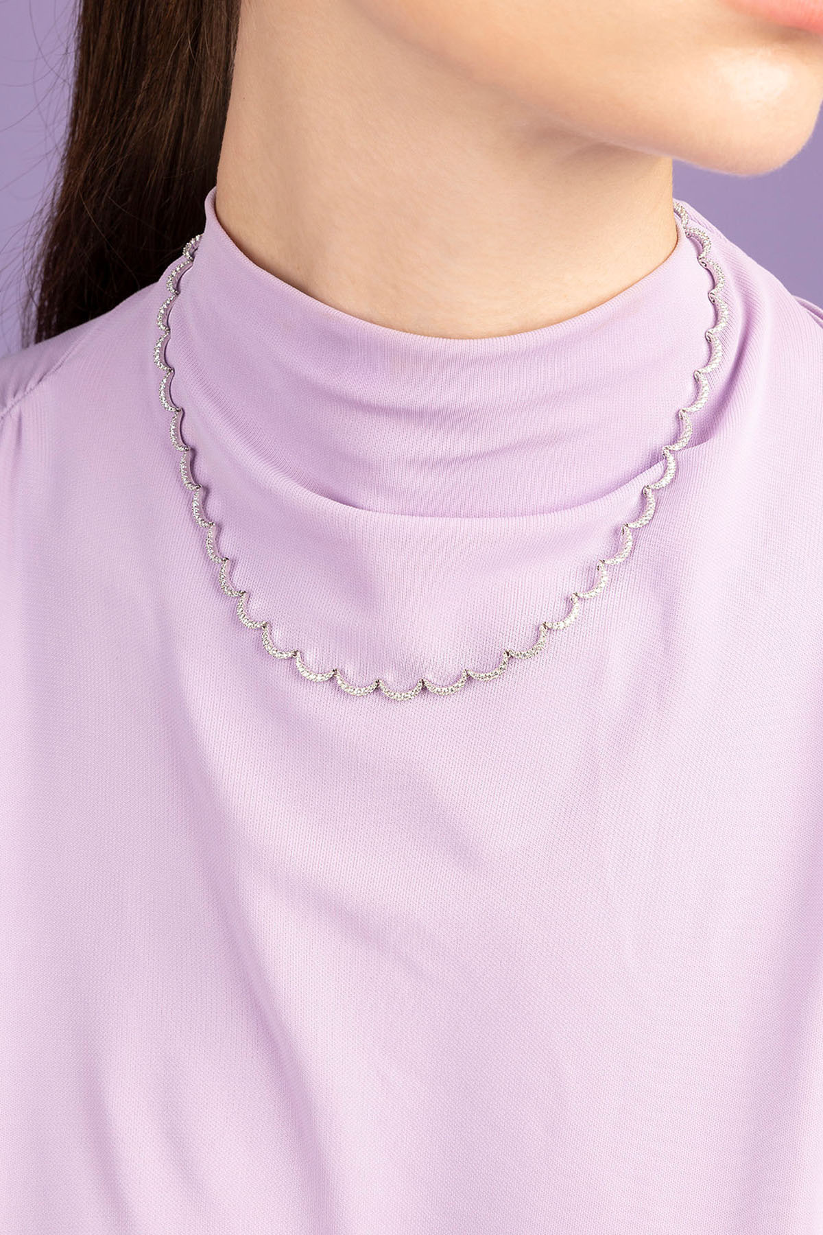Person wearing APM MONACO white wavy chain necklace against a light purple background