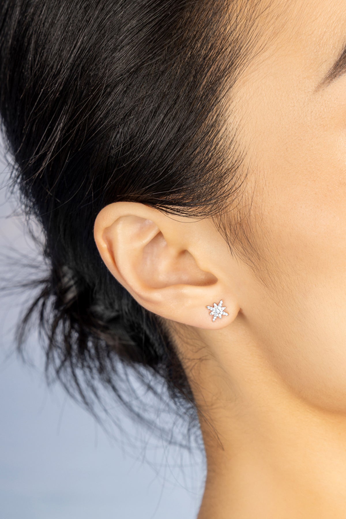 Close-up of an ear wearing APM MONACO butterfly stud earring with a blurred background