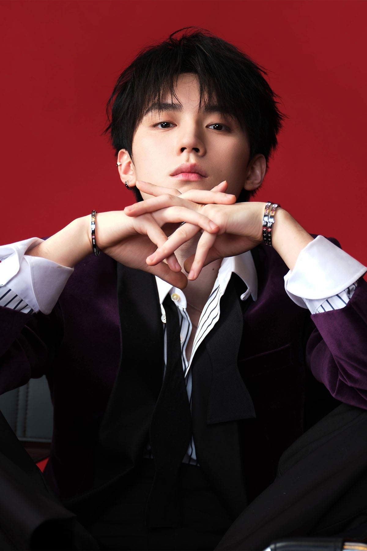 Model wearing a suit with hands clasped in front of a red background with jewelry