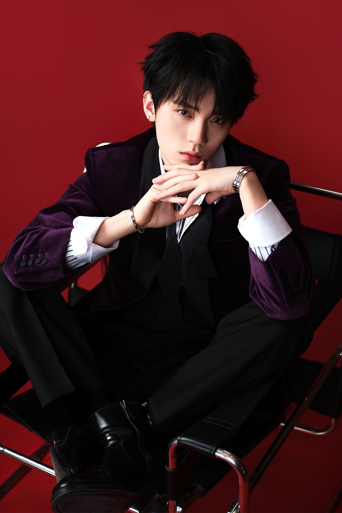 Model wearing a dark suit with jewelry on a red background