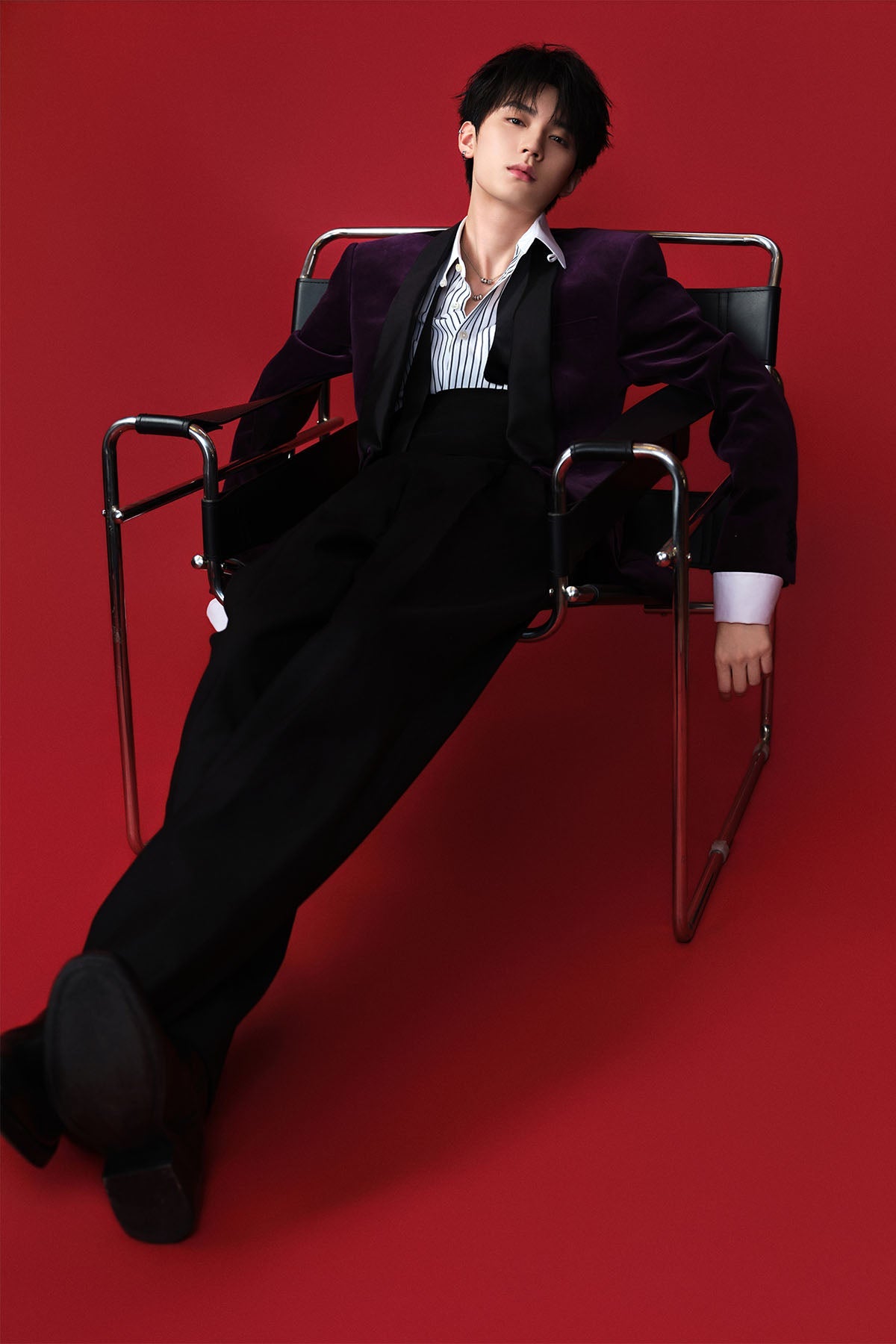 Model in a suit sitting on a chair against a red background