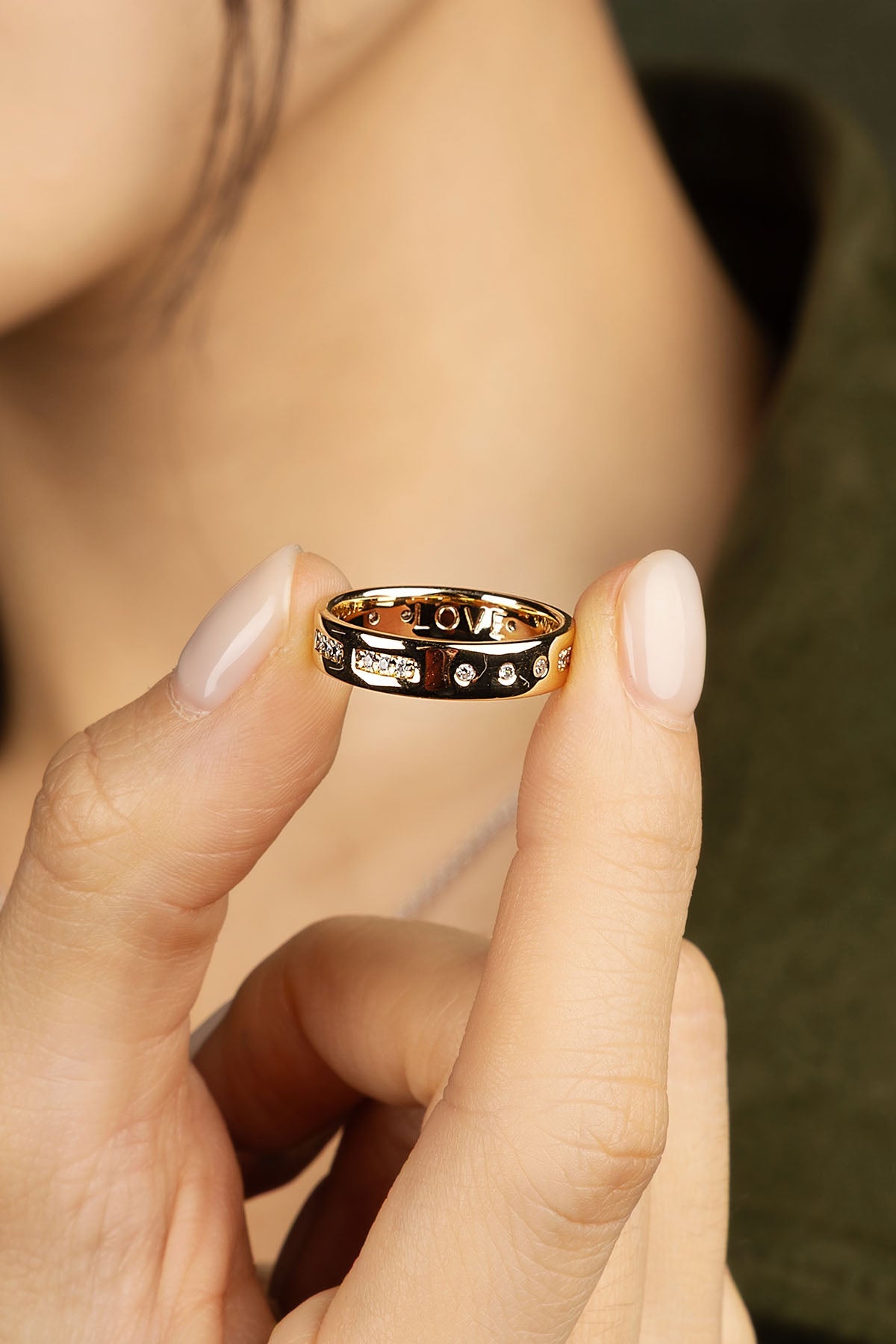 Gold ring with cool design held between fingers against a blurred background