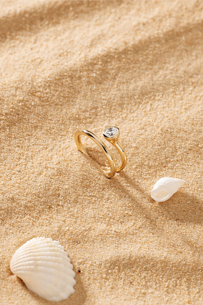 Rings APM Monaco yellow gold twist ring with a clear central stone.