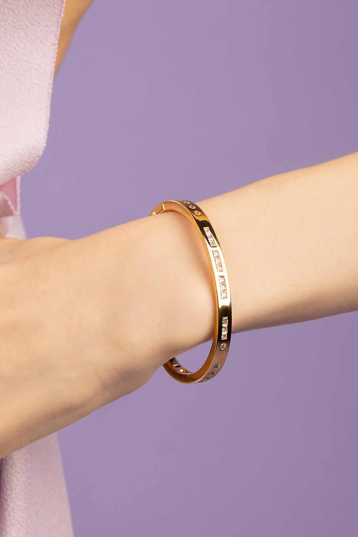 Gold bracelet on a person's wrist against a purple background