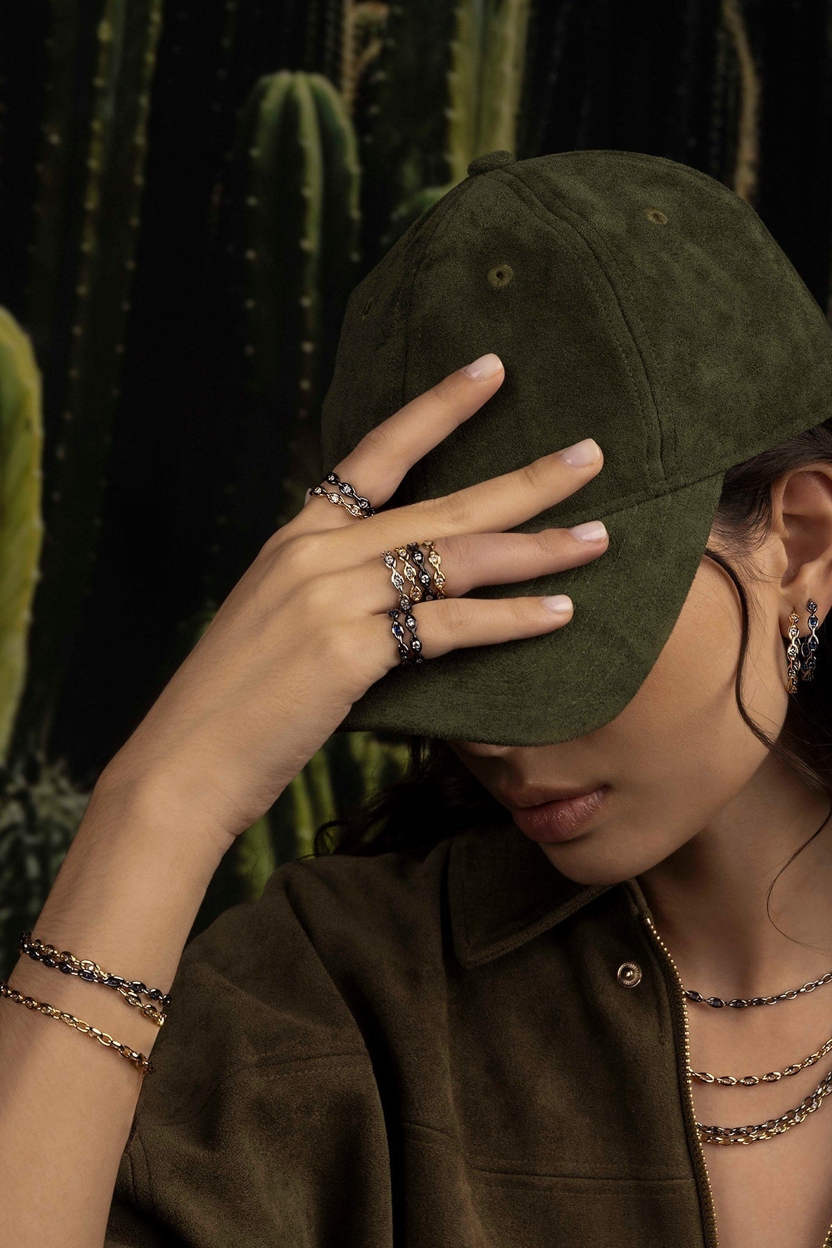 Person wearing a green cap and multiple rings with cacti in the background