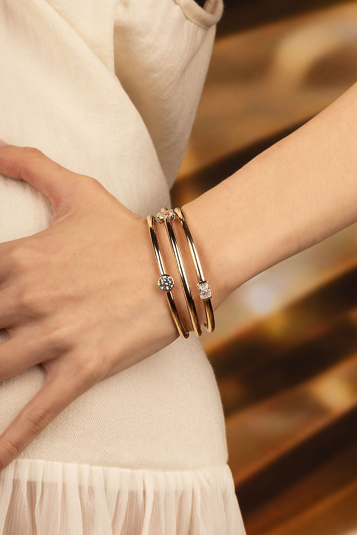 Bracelets APM Monaco: yellow gold triple cuff bangles on a woman's wrist, each with a different-shaped diamond accent.