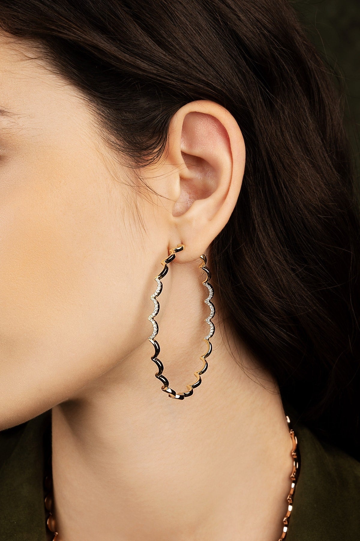 Close-up of an ear wearing a gold hoop earring with a dark background