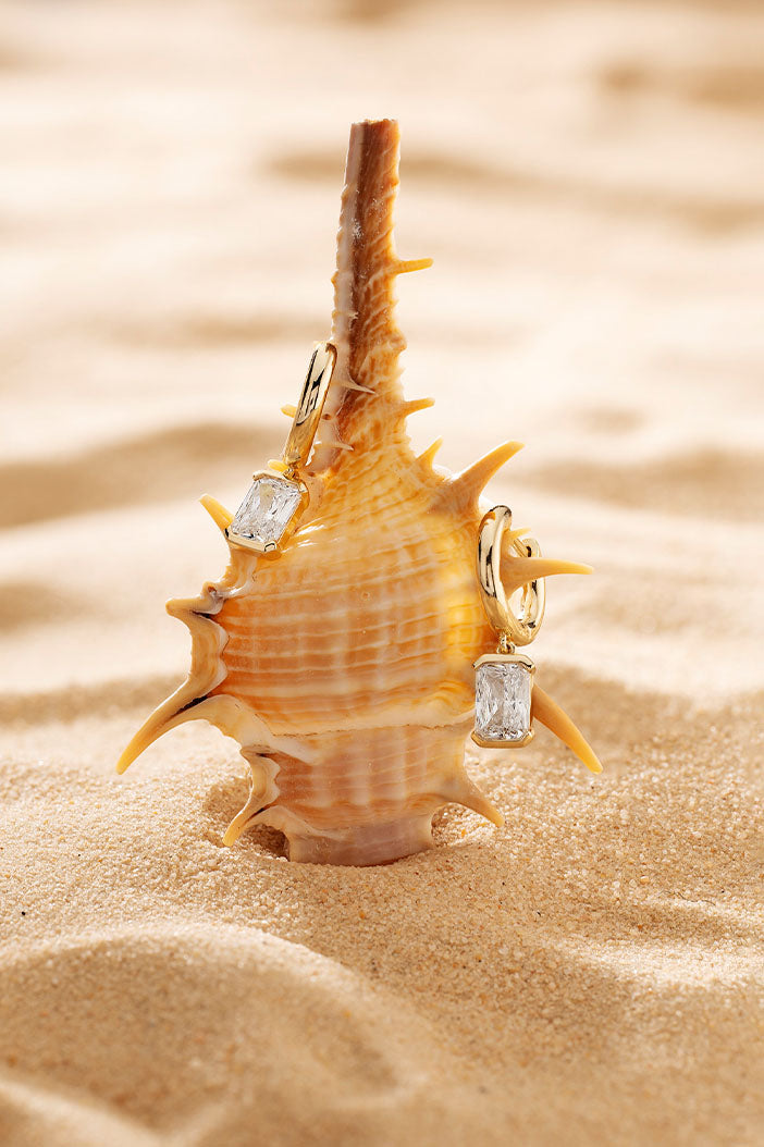 Earrings APM Monaco yellow gold hoop with a rectangular white gemstone.